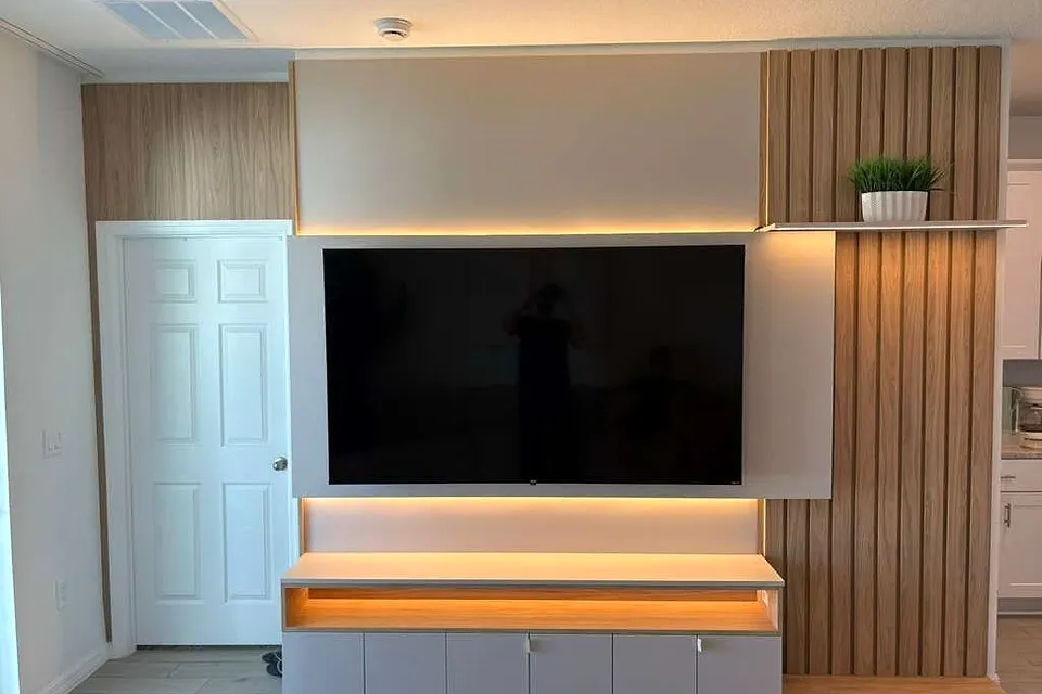 TV wall with a floating white console, lit shelf edge and slatted wood-effect panel