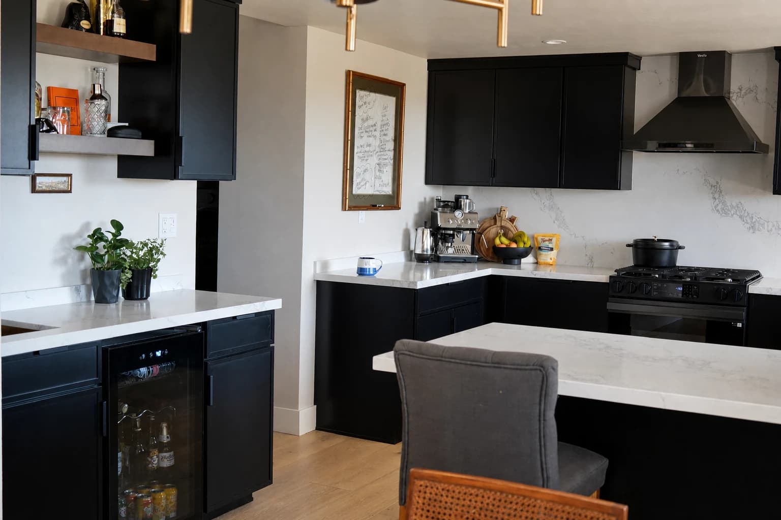 Completed kitchen with black cabinetry, white stone counters, integrated wet bar, and light wood flooring