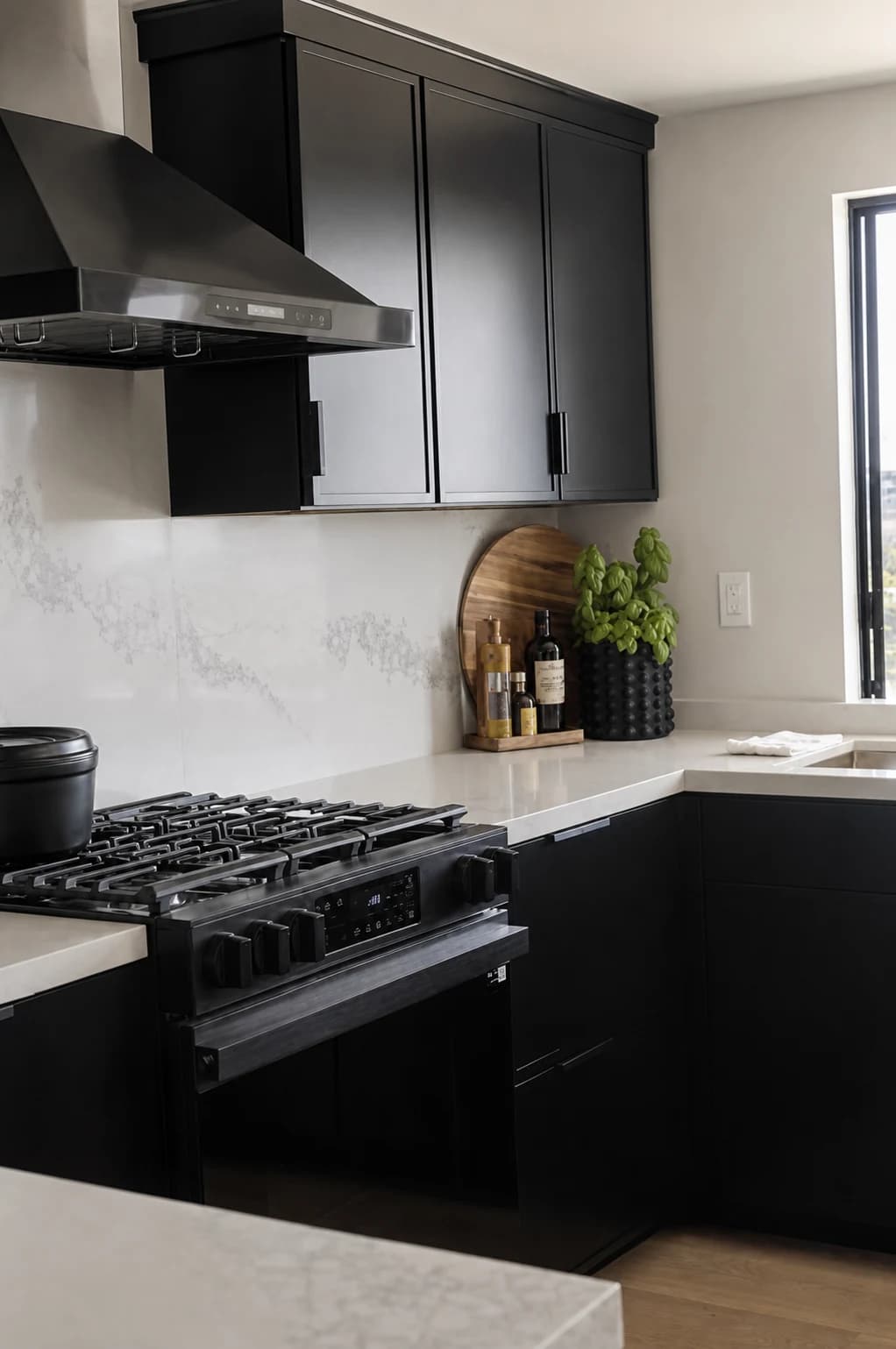 Black kitchen range, hood, cabinetry, and stone backsplash beside a bright window