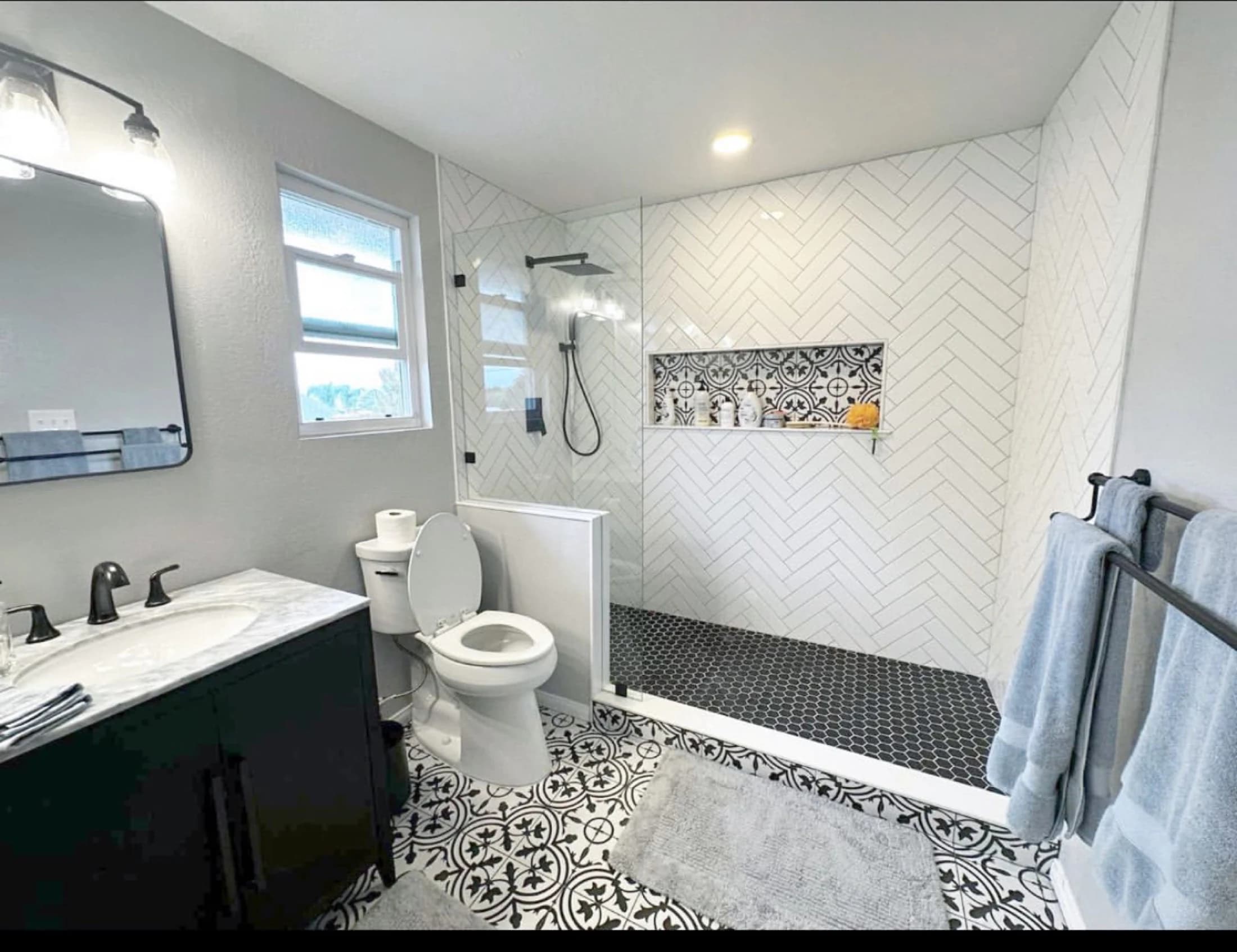 Completed bathroom with a herringbone-tile shower, patterned floor, and dark vanity