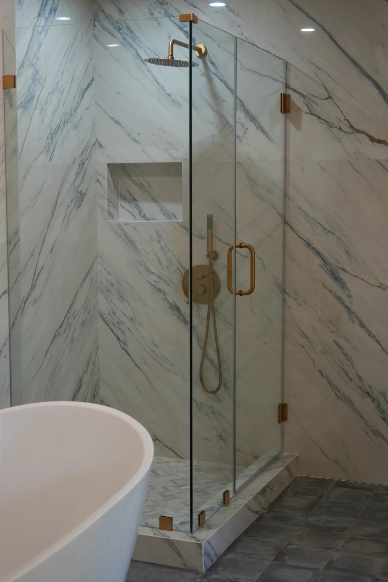 Marble-look shower with frameless glass and warm metal fixtures
