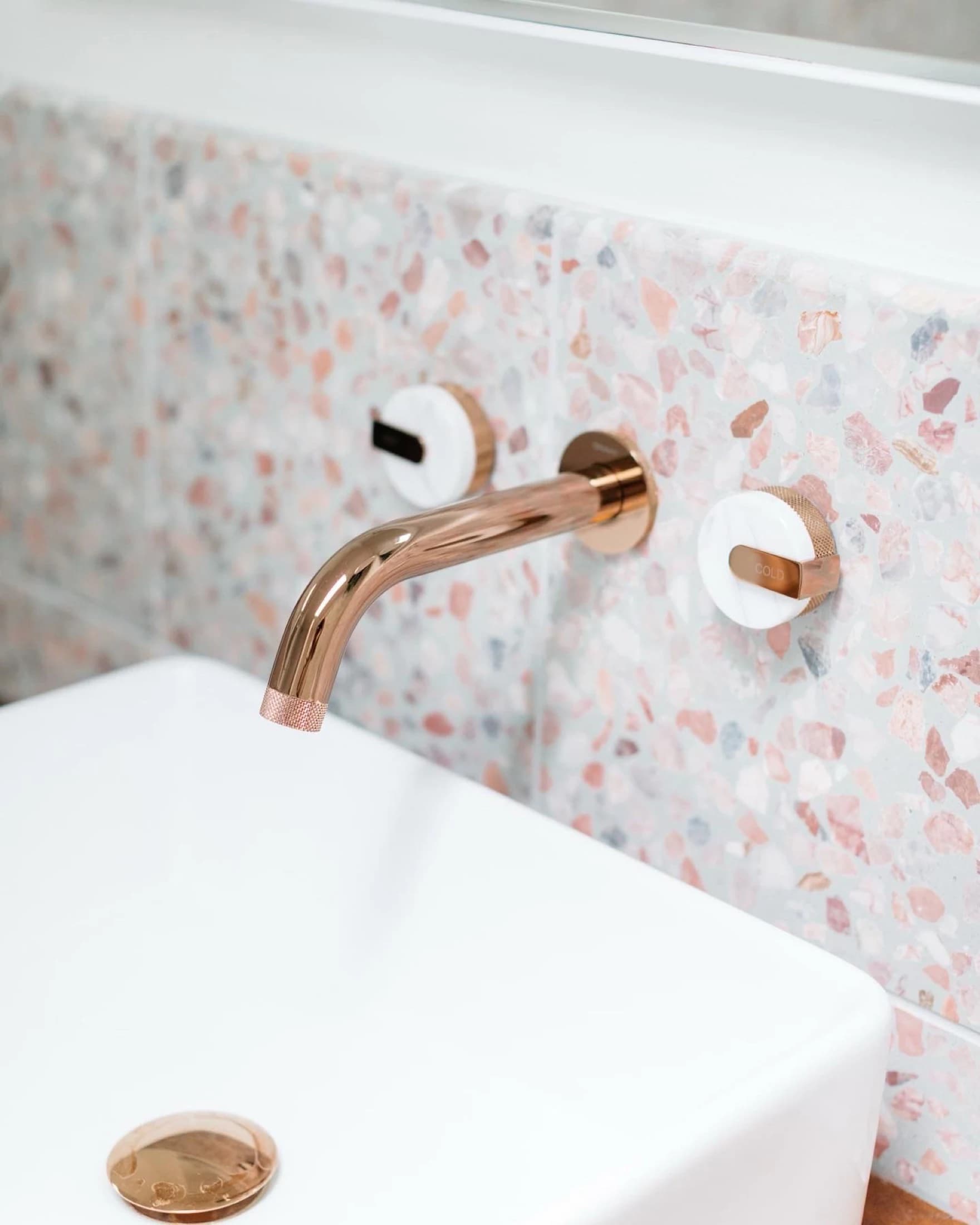 Rose-gold wall-mounted faucet against a terrazzo backsplash