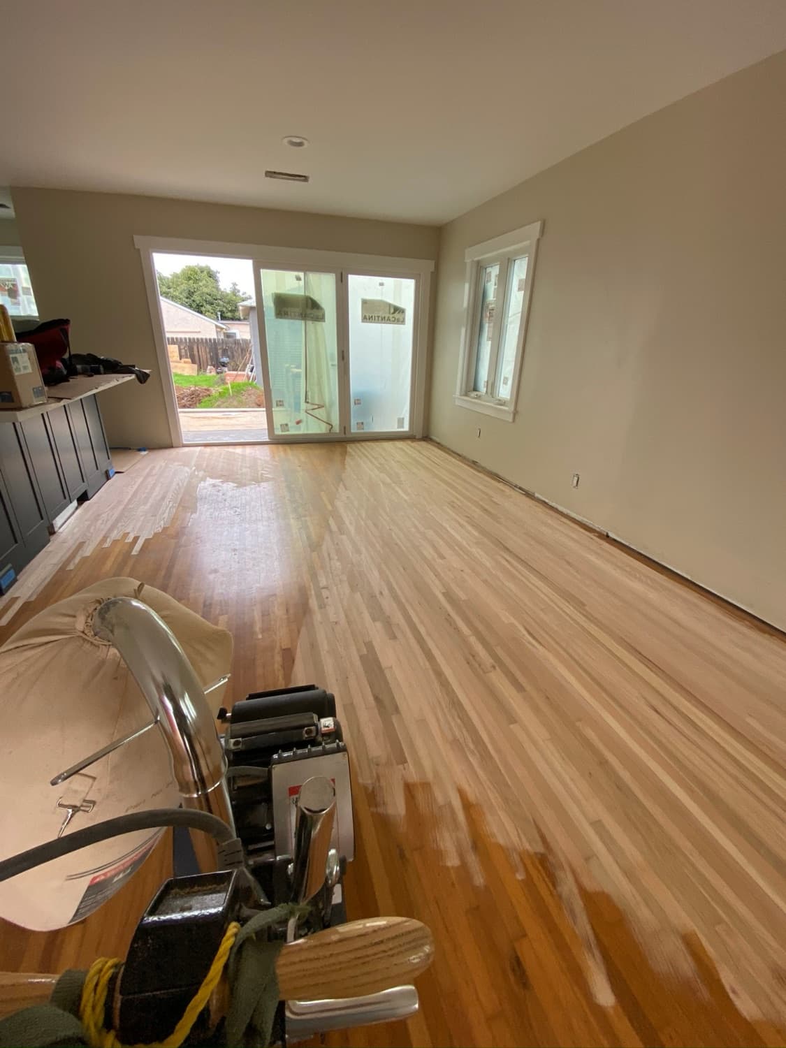 Living room floor sanded to bare wood with the sander in the foreground