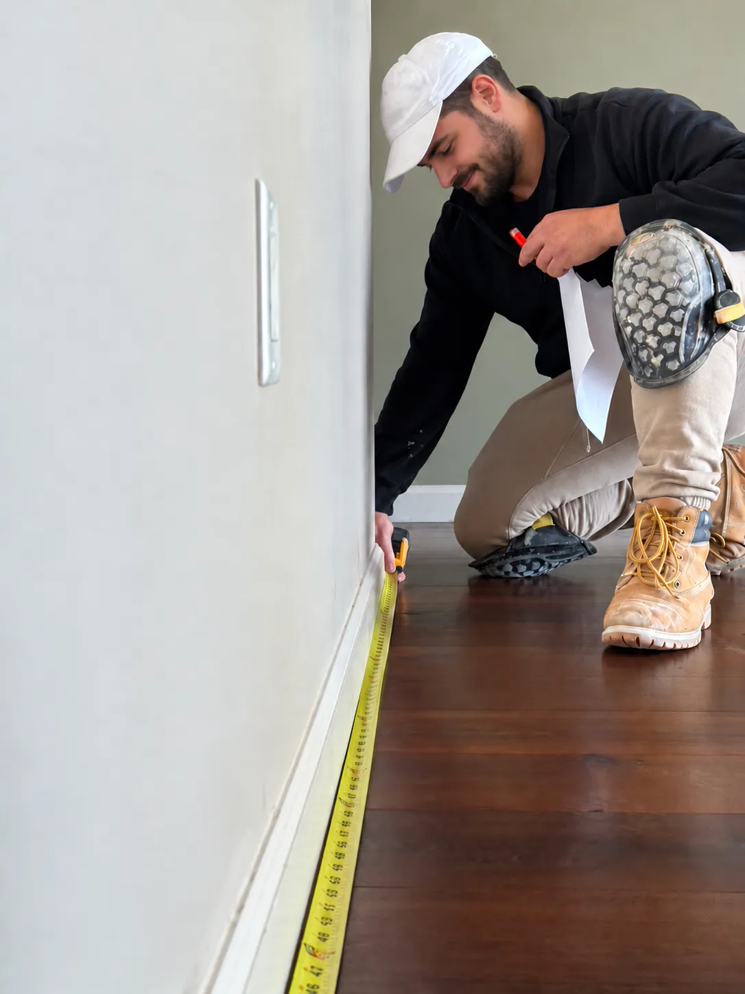 Crew member measuring a dark wood floor along the baseboard