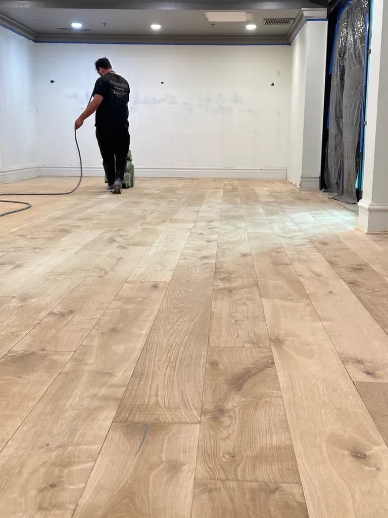 Crew member sanding a wide plank floor in an empty room