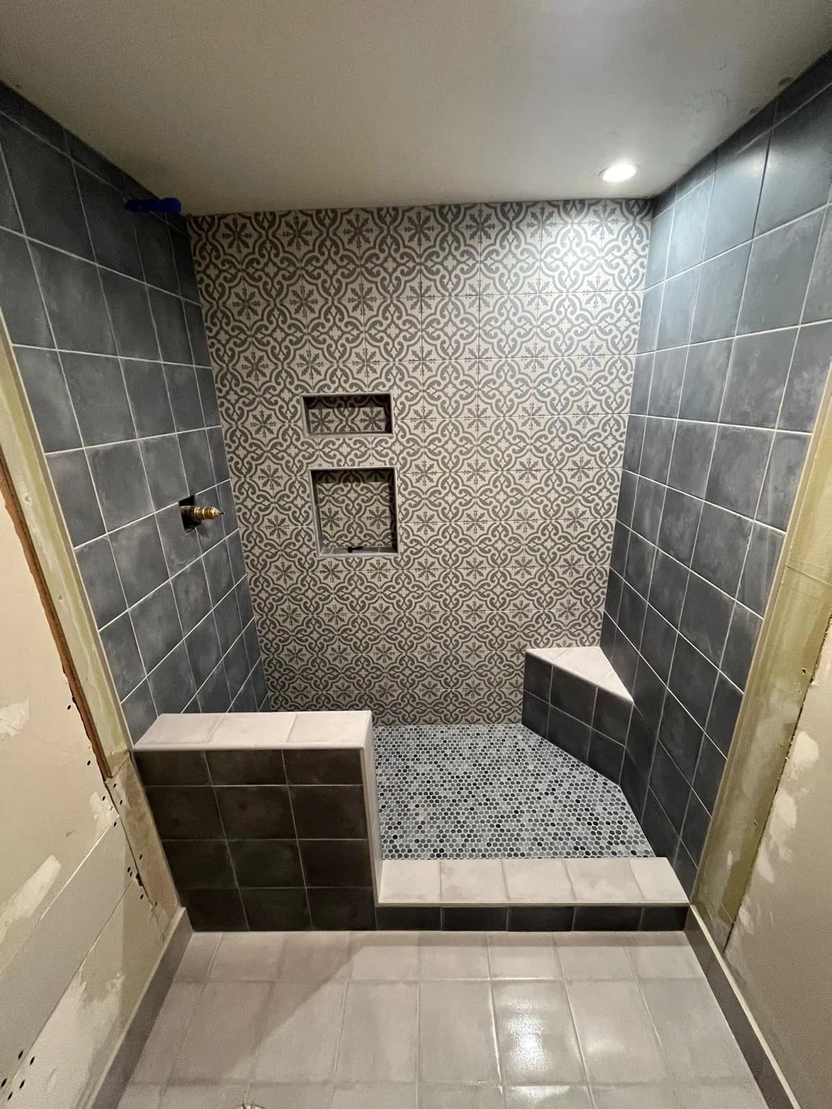 Walk-in shower with a patterned tile wall, two niches and a corner bench
