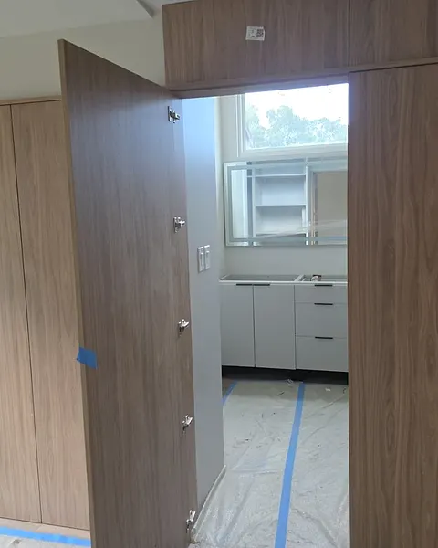 Full-height wood-effect door opened in a paneled wall, with a kitchen visible behind