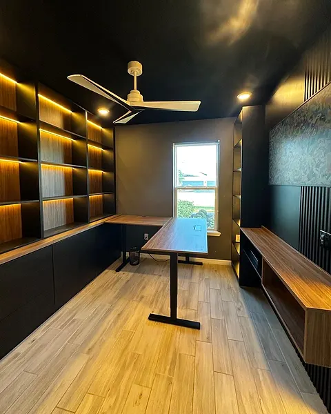 Home office with dark cabinetry, lit wood shelving and a standing desk