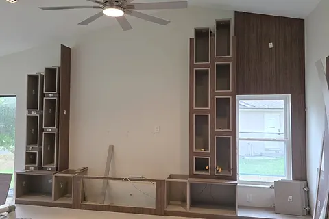Stepped wood-effect shelving and a tall panel being installed beside a window