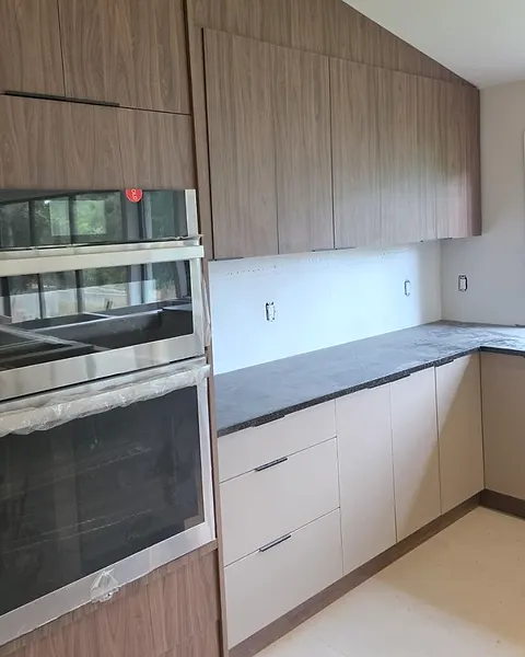 Wall oven tower in wood-effect cabinetry beside light base drawers and a dark stone counter