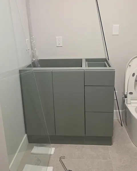 Sage green vanity base with doors and drawers set in a bathroom, before the countertop