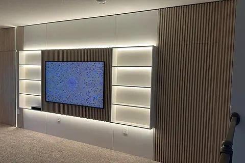 Media wall with lit shelves on both sides of a screen and slats to the right
