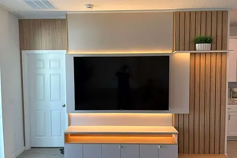 TV wall with a floating white console, lit shelf edge and slatted wood-effect panel