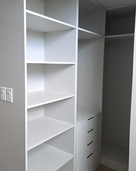 White closet tower with open shelves and drawers inside a walk-in closet