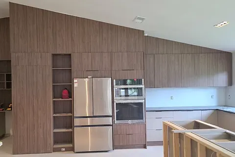 Wood-effect cabinet wall rising to a sloped ceiling in an open kitchen, shown during installation