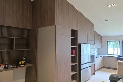 Wood-effect wall unit with slatted shelves and a built-in desk niche next to an open kitchen